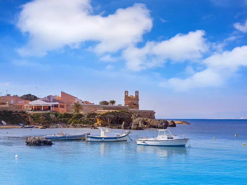 View of Tabarca Island from the sea with boats anchored in crystal-clear waters and the historic fortress in the background, near Alicante.