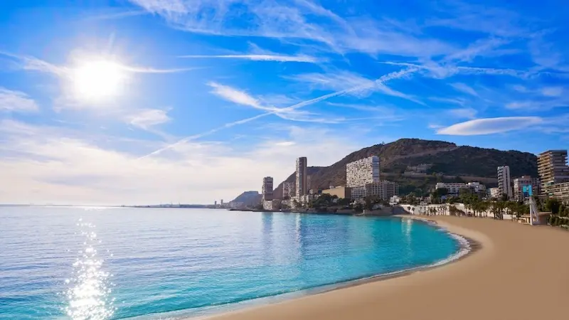 Playa de la Albufereta in Alicante with calm turquoise waters and city buildings along the shore