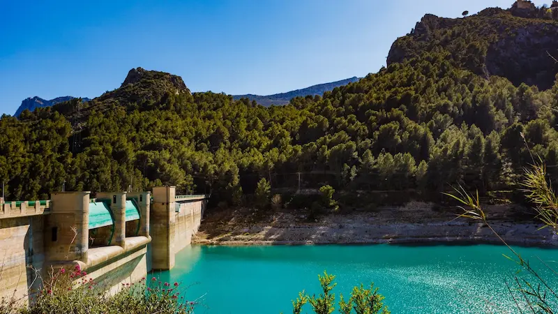 View of the turquoise Guadalest reservoir surrounded by pine-covered mountains on the Costa Blanca, near Alicante, Spain